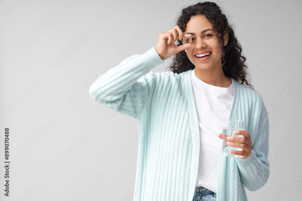 Young African-American woman taking fish oil on grey background Young African-American woman taking fish oil on grey background