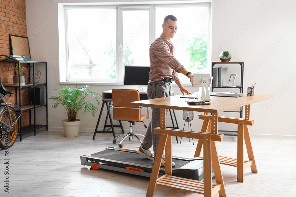 Young businessman working with tablet computer on treadmill at table in office Young businessman working with tablet computer on treadmill at table in office