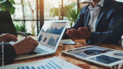 Two diverse business men discussing financial market data using laptop and digital tablet. Financial advisor broker manager consulting investor client about digital investment - generative ai