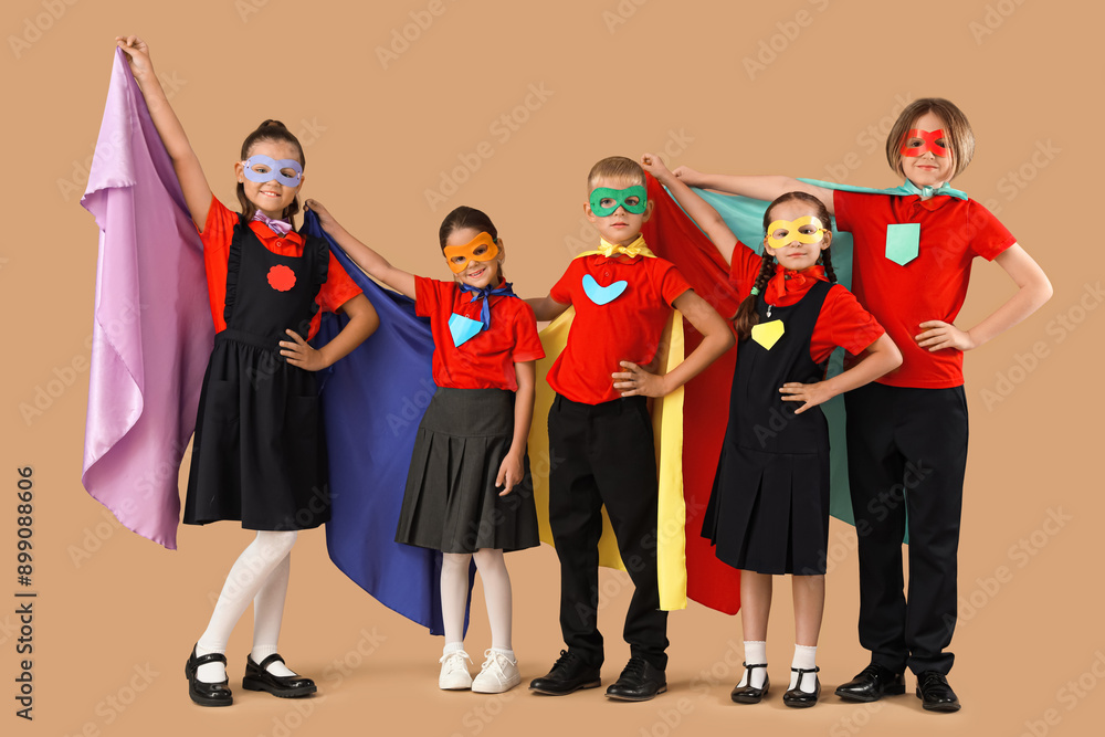 Happy pupils dressed as superheroes on brown background Happy pupils dressed as superheroes on brown background