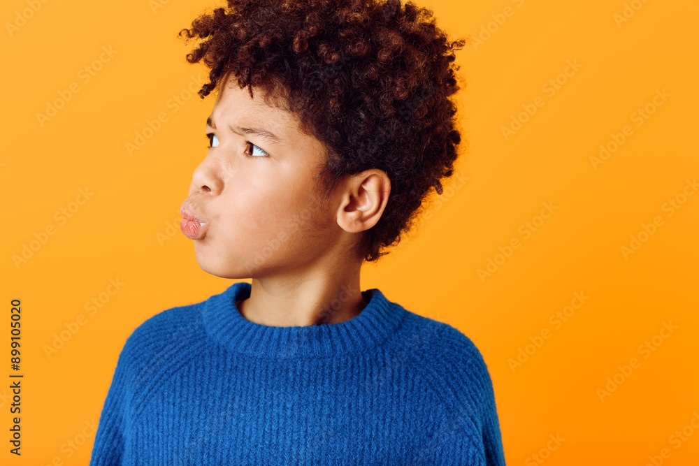 Cheerful young boy with vibrant afro making silly faces against a bright orange backdrop in playful expression Cheerful young boy with vibrant afro making silly faces against a bright orange backdrop in playful expression