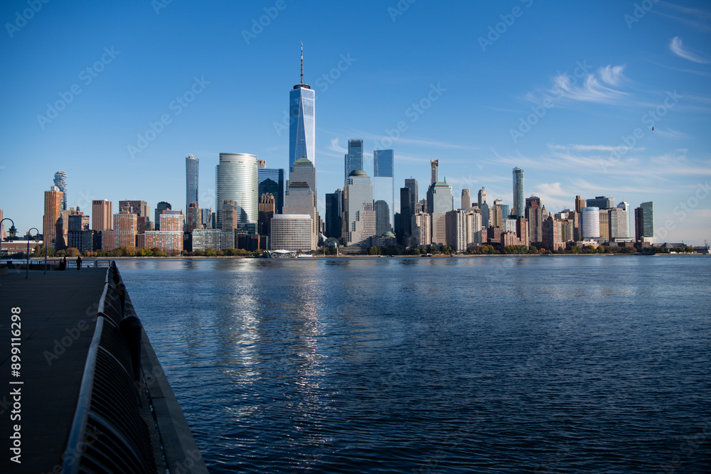 Obraz premium Lower Manhattan and One World Trade Center in New York City, USA as seen from Weehawken New Jersey. Skyscrapers of Manhattan located near rippling water of New York bay against blue sky.
