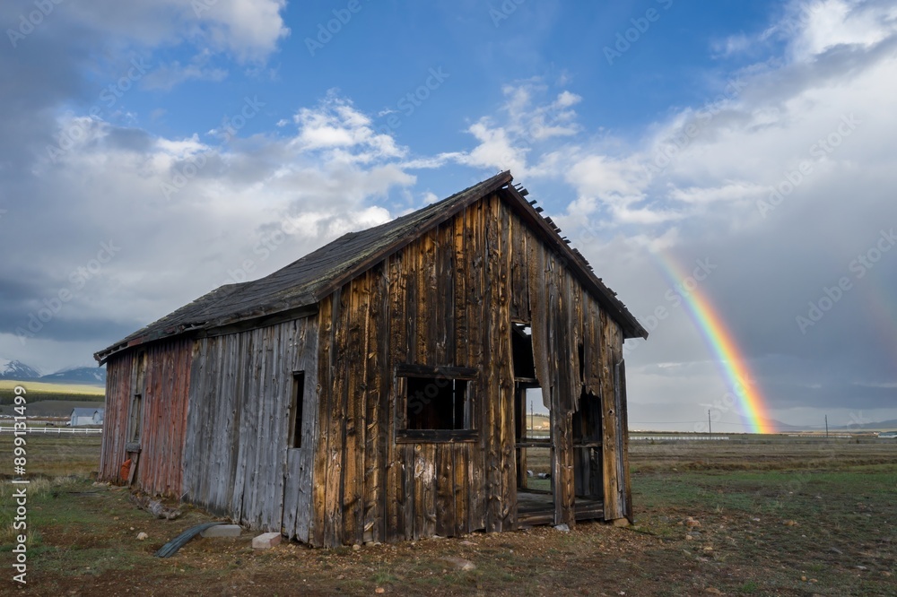 Abandoned wooden barn in the countryside. Behind it is a large rainbow. Leadville, Colorado, United States of America. Abandoned wooden barn in the countryside. Behind it is a large rainbow. Leadville, Colorado, United States of America.