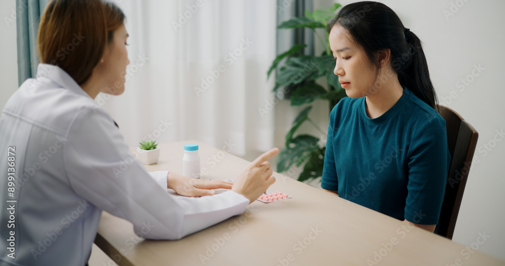 High angle view, Asian doctor explaining how to take medicine to young female patient in clinic office, Health and medicine consultant, Conversation about healthcare High angle view, Asian doctor explaining how to take medicine to young female patient in clinic office, Health and medicine consultant, Conversation about healthcare