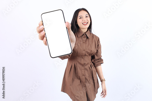 Smiling beautiful young Asian woman wearing casual brown showing a screen mobile phone for an advertisement and presenting isolated over white background. People Lifestyle Concept