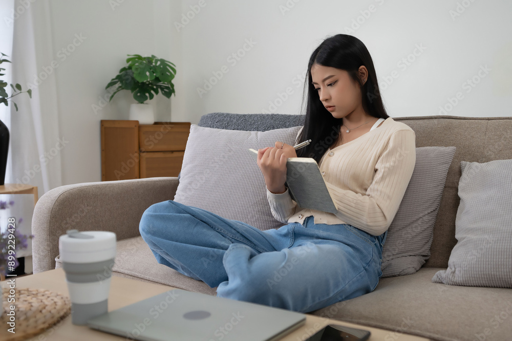 Young asian women reading the book to analysis information and writing notes while sitting on comfortable couch to learning self-study and spending time to relaxation with enjoying lifestyle at home Young asian women reading the book to analysis information and writing notes while sitting on comfortable couch to learning self-study and spending time to relaxation with enjoying lifestyle at home