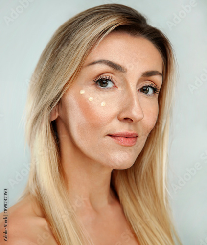 Beautiful gorgeous 50s mid middle aged mature woman with three dots of eye cream on face isolated on white background. Mature european lady portrait. Old Age Concept for Skincare, Cosmetics Product photo