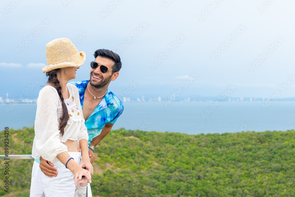 Obraz premium Happy Caucasian family couple enjoy outdoor lifestyle travel tropical island on summer beach holiday vacation. Husband and wife relaxing on mountain peak and looking beautiful nature of the sea.