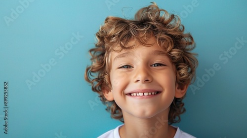 Wallpaper Mural Golden Curls, Brighter Smile: A young boy beams at the camera, his infectious joy radiating against a vibrant blue backdrop.  Torontodigital.ca