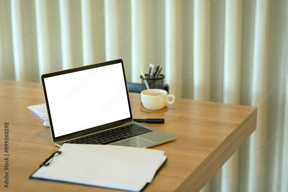 Laptop with white empty display, clipboard, coffee cup and stationery on wooden office desk Laptop with white empty display, clipboard, coffee cup and stationery on wooden office desk