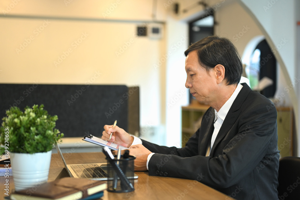 Mature businessman in black suit working with laptop and documents in a modern office Mature businessman in black suit working with laptop and documents in a modern office