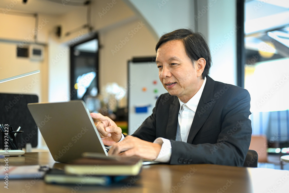 Smiling senior businessman in black suit analyzing financial data on laptop screen Smiling senior businessman in black suit analyzing financial data on laptop screen