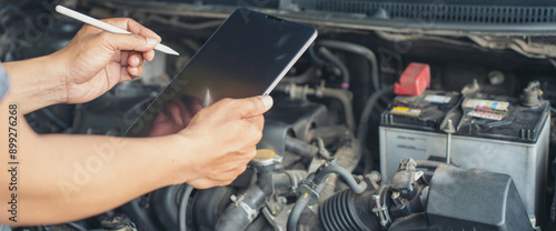 Close-up of Car mechanic noting repair parts during open car hood engine repair unrecognisable man wearing gray glove inspecting car engine and interior of hood of car. at garage. 