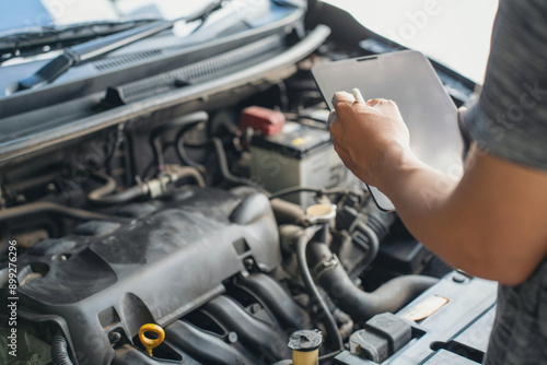 Close-up of Car mechanic noting repair parts during open car hood engine repair unrecognisable man wearing gray glove inspecting car engine and interior of hood of car. at garage.