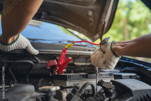 Close-up of mechanic holding voltmeter to check voltage car battery energy problem for service maintenance. Car mechanic noting repair parts during open car hood engine repair unrecognisable photo