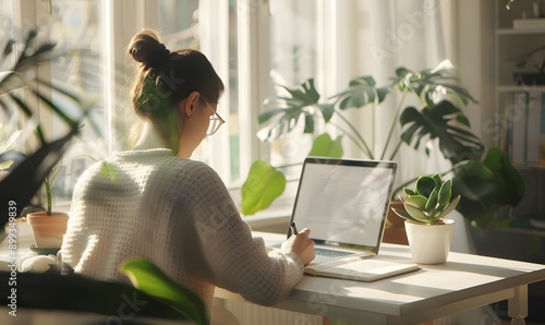 A woman sitting at a table with a laptop open next to her and writing in a notebook, Generative AI