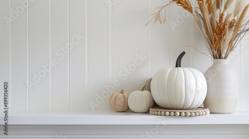 A minimalist mantel decorated with a single white pumpkin and a few sprigs of dried wheat