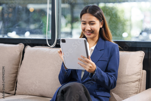 An Asian businesswoman sits at a table, working with a smile. She manages her online Kuya business with enthusiasm, showcasing her dedication and positive attitude while handling tasks efficiently.