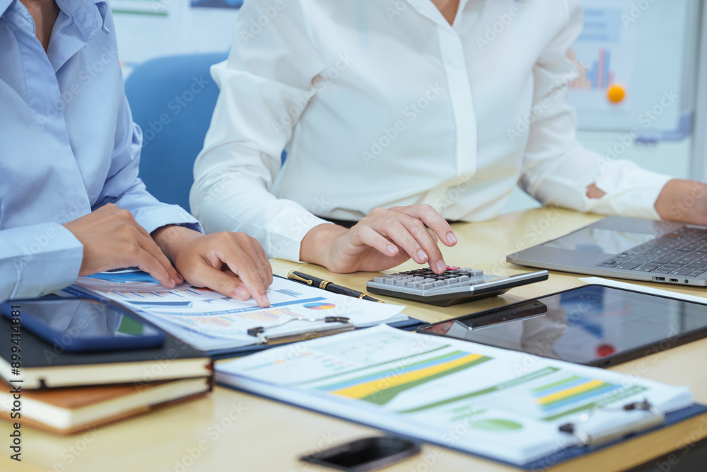 Two young Asian businesswomen sit at a table, engaged in a meeting.examine graphs and discuss capital investment strategies, showcasing their expertise and collaborative approach to business growth. Two young Asian businesswomen sit at a table, engaged in a meeting.examine graphs and discuss capital investment strategies, showcasing their expertise and collaborative approach to business growth.