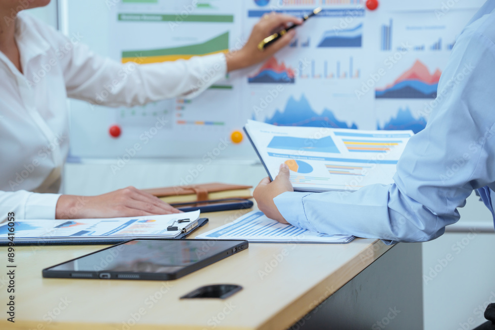 Two young Asian businesswomen sit at a table, engaged in a meeting.examine graphs and discuss capital investment strategies, showcasing their expertise and collaborative approach to business growth. Two young Asian businesswomen sit at a table, engaged in a meeting.examine graphs and discuss capital investment strategies, showcasing their expertise and collaborative approach to business growth.