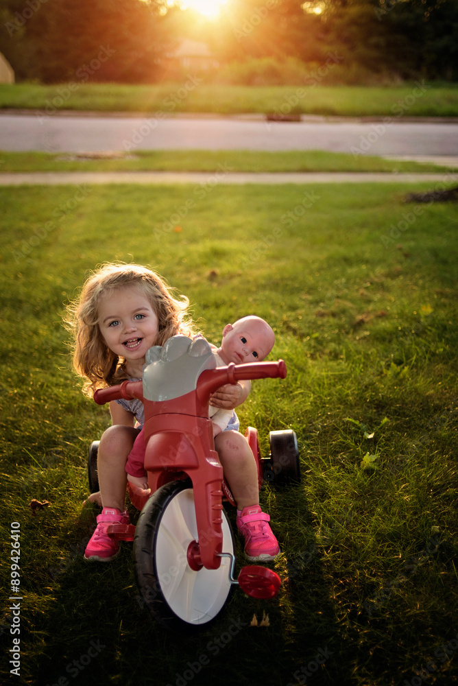 Young girl on red bike with baby doll at sunset Young girl on red bike with baby doll at sunset