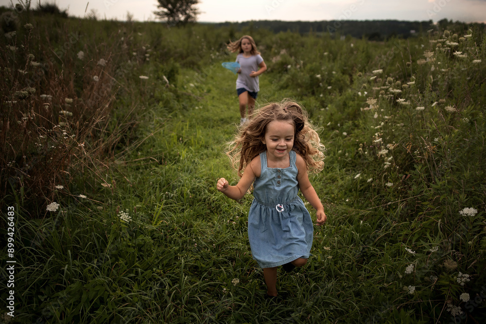 Young sisters running through wildflower field in summer Young sisters running through wildflower field in summer