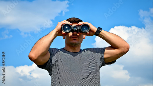 Man Looking Through Binoculars Against Blue Sky, Outdoor Exploration and Adventure Concept, Stock Photograph