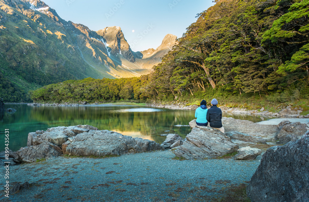 Couple sitting on the rocks and enjoying the views of Lake Mackenzie at Routeburn Track at sunset. South Island. New Zealand.