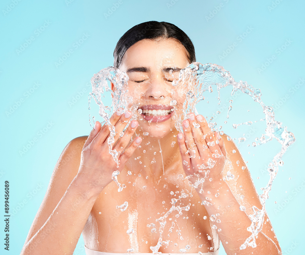 Happy, woman and splash or water in studio for skincare, dermatology and glow or wellness. Hygiene, model girl and smile of hands with liquid for facial and aesthetic or shine by blue background Happy, woman and splash or water in studio for skincare, dermatology and glow or wellness. Hygiene, model girl and smile of hands with liquid for facial and aesthetic or shine by blue background