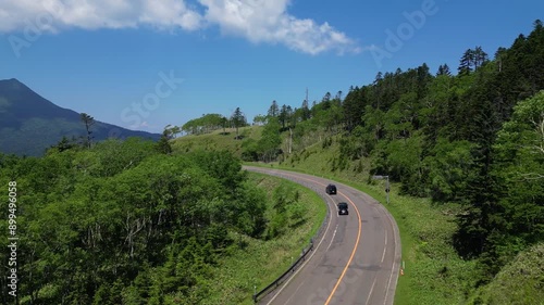 Hokkaido, Japan: Aerial drone footage following cars on the road in the Akan-Mashu National Park with the Mount Oakan volcano in the background in Hokkaido in summer in Japan.  photo