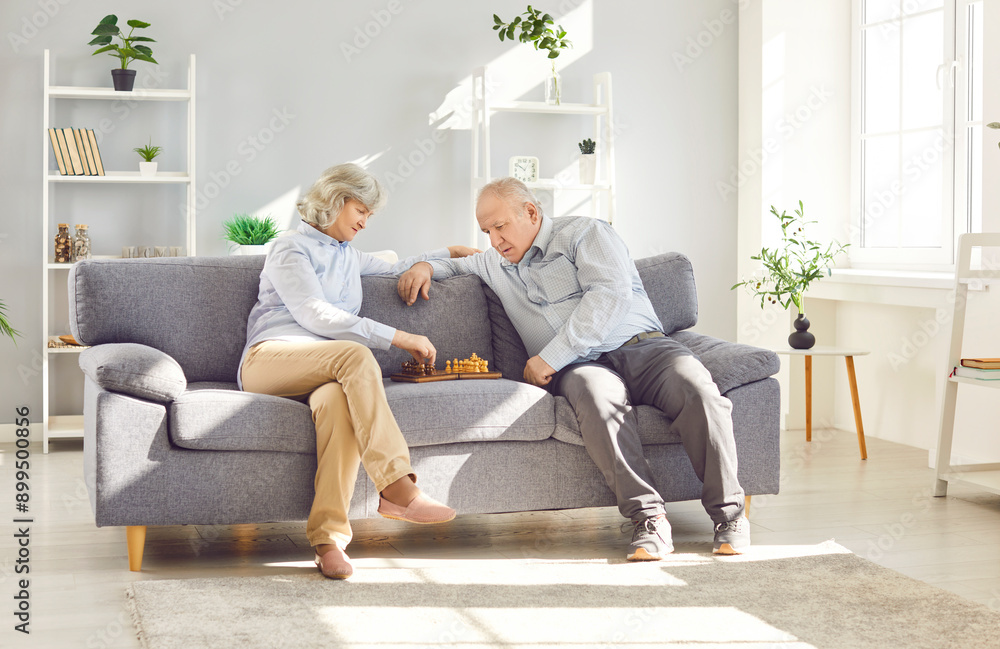 Portrait of senior old couple playing chess together sitting on sofa in living room at home. Retired elderly man and woman playing board games enjoying retirement. Family leisure concept. Portrait of senior old couple playing chess together sitting on sofa in living room at home. Retired elderly man and woman playing board games enjoying retirement. Family leisure concept.