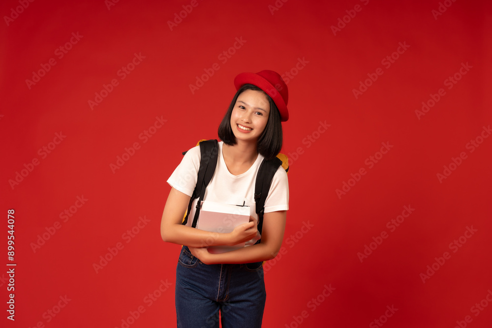 The red studio background reflects the Asian school girl's eagerness to learn, representing her commitment to academic excellence and personal development, holding books and a school bag. The red studio background reflects the Asian school girl's eagerness to learn, representing her commitment to academic excellence and personal development, holding books and a school bag.