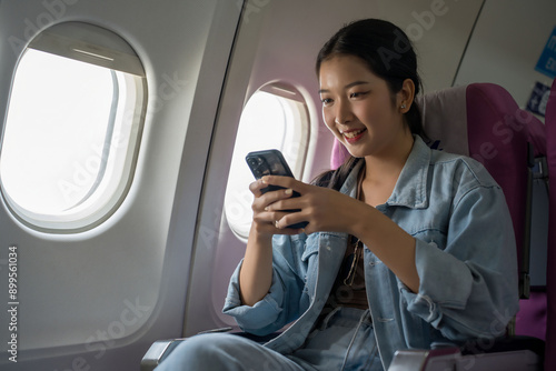 Asian traveler women use smartphone surfing social media with entertainment and typing message chat while sitting near windows during flight business travel in airplane with vacation time lifestyle photo