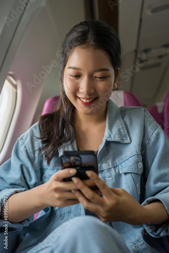 Asian traveler women using smartphone to surfing social media and watching the movie entertainment while sitting near windows during flight business travel in airplane with vacation time lifestyle