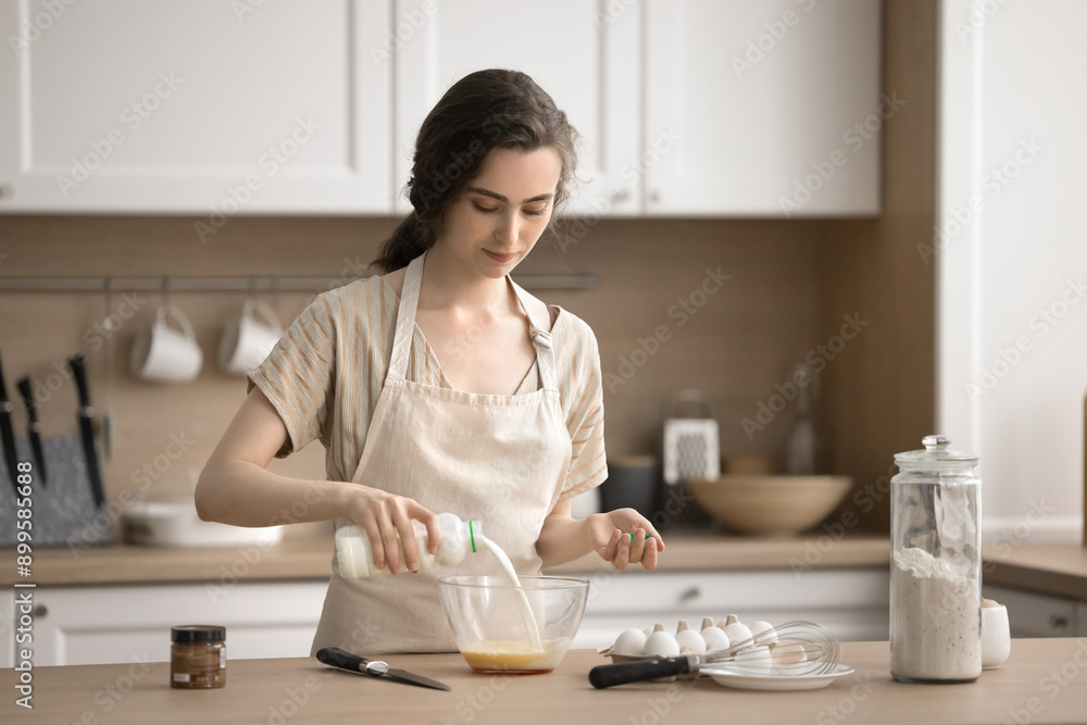 Young female pouring milk into bowl of beaten eggs, prepare omelet or dough for pastries, making homemade dish, enjoy process and homemade cookery process, trying new recipe. Routine, household chores Young female pouring milk into bowl of beaten eggs, prepare omelet or dough for pastries, making homemade dish, enjoy process and homemade cookery process, trying new recipe. Routine, household chores