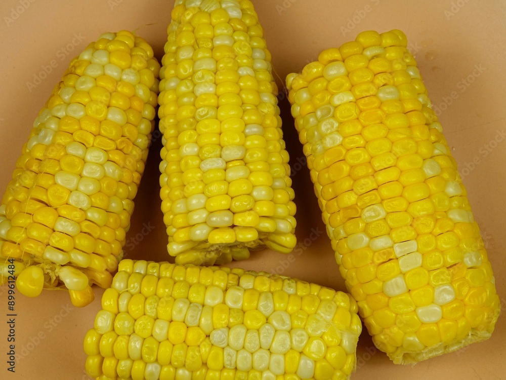 Sweet yellow fresh boiled corn cobs are on an orange plate Sweet yellow fresh boiled corn cobs are on an orange plate