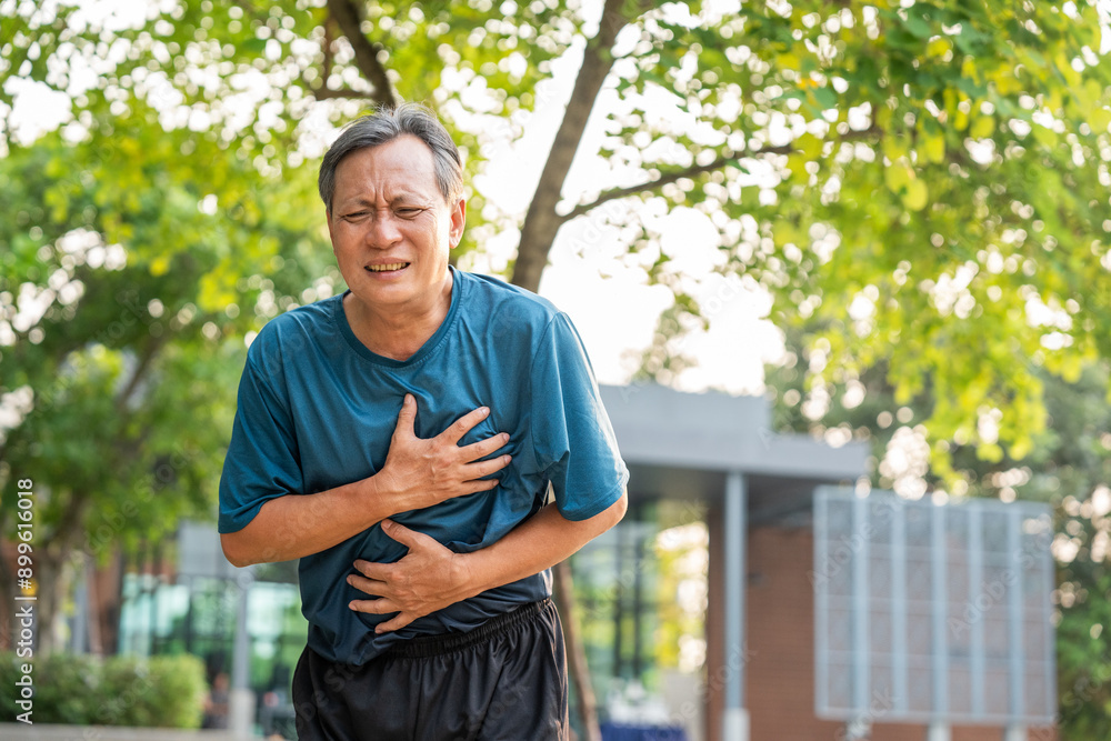 Obraz premium Senior asian man tired during jogging at outdoor nature park. Mature asian male intense training workout challenge breathing exhausted. Healthy and activity lifestyle concept.