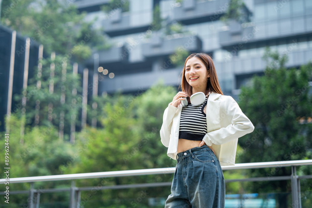 Fototapeta premium Young asian woman fashion lifestyle with headphone standing posing in urban city downtown. Happy attractive charming asian female living in city. People and lifestyle.
