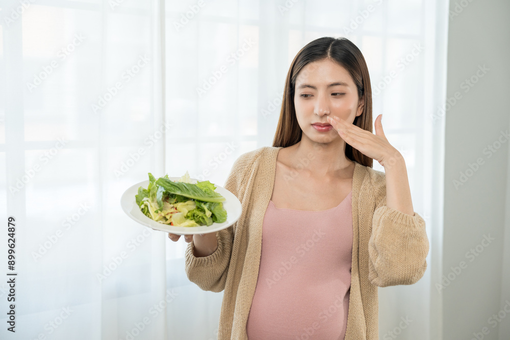 Unhappy young asian pregnant woman feeling with morning sickness to vegetable salad, frustrated young lady refusing eating vegetable, concept of hate vegetarian nutrition Unhappy young asian pregnant woman feeling with morning sickness to vegetable salad, frustrated young lady refusing eating vegetable, concept of hate vegetarian nutrition