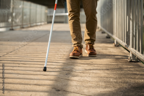 Young blind man walking in city with walking stick. Visually impaired man difficult to traveling on the road wearing sun glasses Cross the road cross the footbridge photo