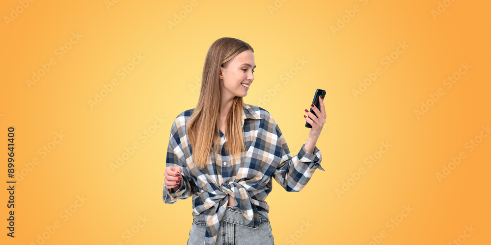 Smiling young woman with phone in hand, empty orange background Smiling young woman with phone in hand, empty orange background