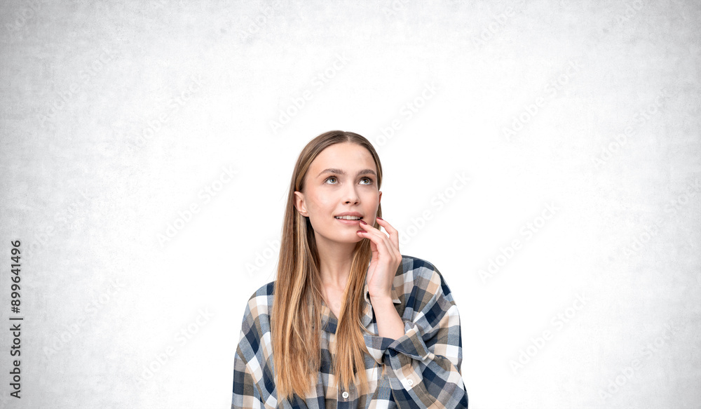 A young woman wearing a checkered shirt looks up thoughtfully, t A young woman wearing a checkered shirt looks up thoughtfully, t