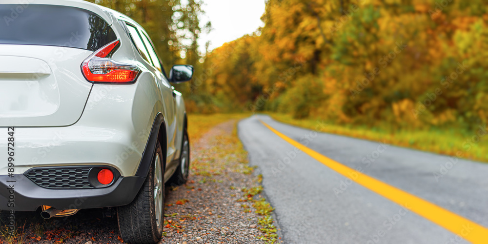 A white car is parked on the side of a country highway.