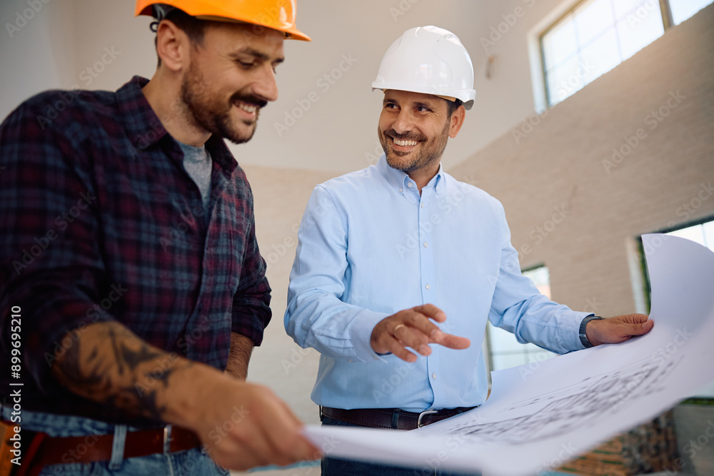 Happy housing project manager examining blueprints with worker at construction site. Happy housing project manager examining blueprints with worker at construction site.