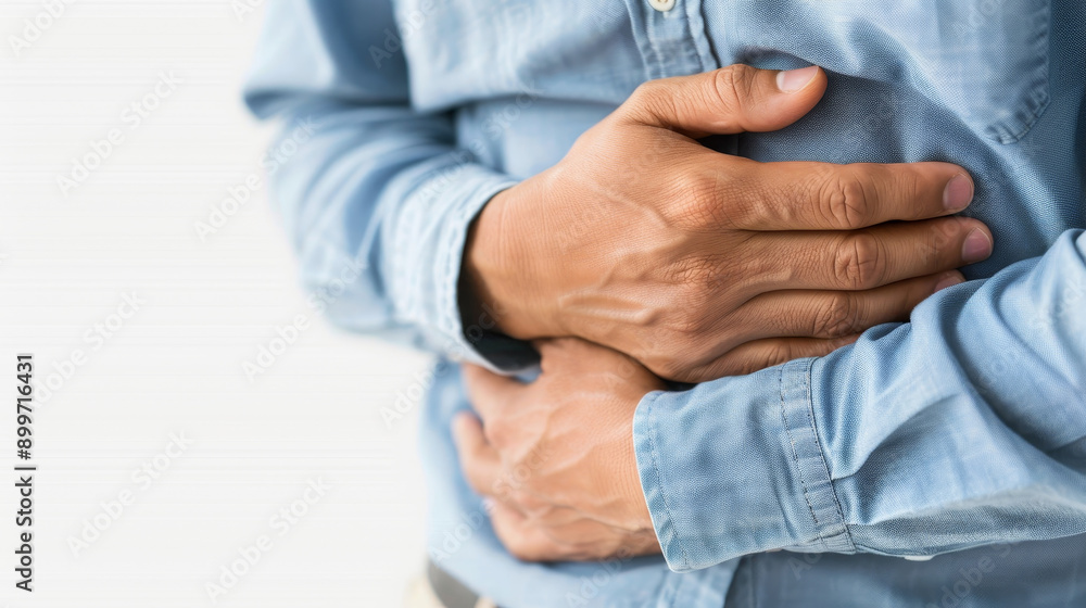 A person with a hand on their stomach, indicating discomfort or pain, wearing a casual blue shirt in a neutral backdrop. A person with a hand on their stomach, indicating discomfort or pain, wearing a casual blue shirt in a neutral backdrop.