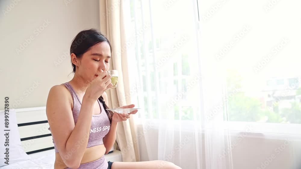 Portrait asian woman in sports bra drinking warm herbal tea by bedroom window in warm sunlight on a morning : Healthy tea concept Portrait asian woman in sports bra drinking warm herbal tea by bedroom window in warm sunlight on a morning : Healthy tea concept