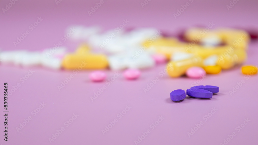 Violet pills placed on a pink background with blurred assorted pharmatheutical multicolored medicinal capsules and pills. Painkillers, antibiotics variation, medical treatment concept, space for text. Violet pills placed on a pink background with blurred assorted pharmatheutical multicolored medicinal capsules and pills. Painkillers, antibiotics variation, medical treatment concept, space for text.