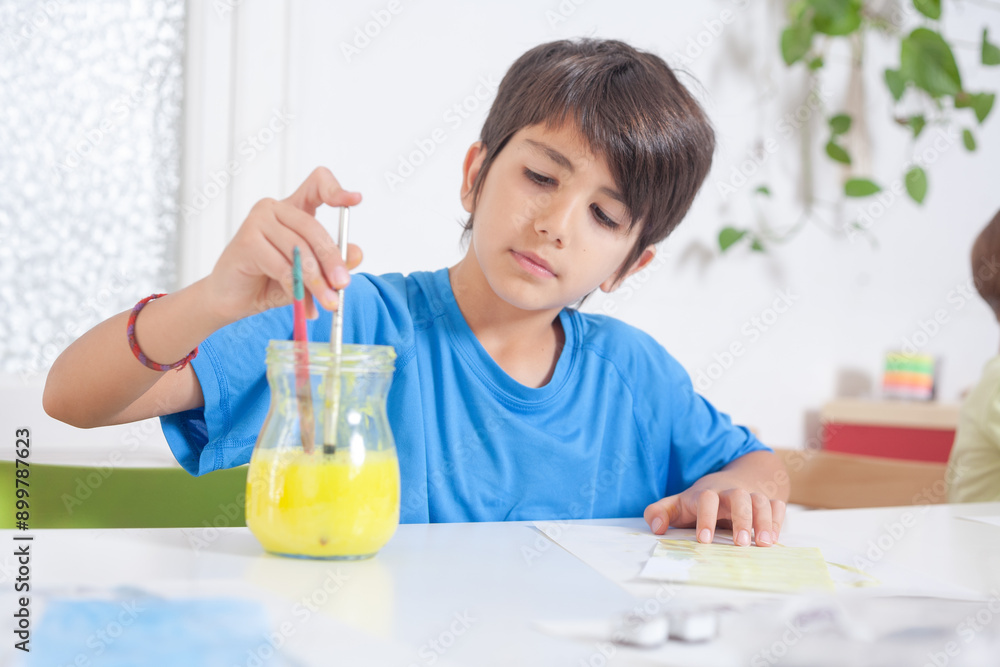 Kid dips paintbrush in water during watercolor painting craft Kid dips paintbrush in water during watercolor painting craft