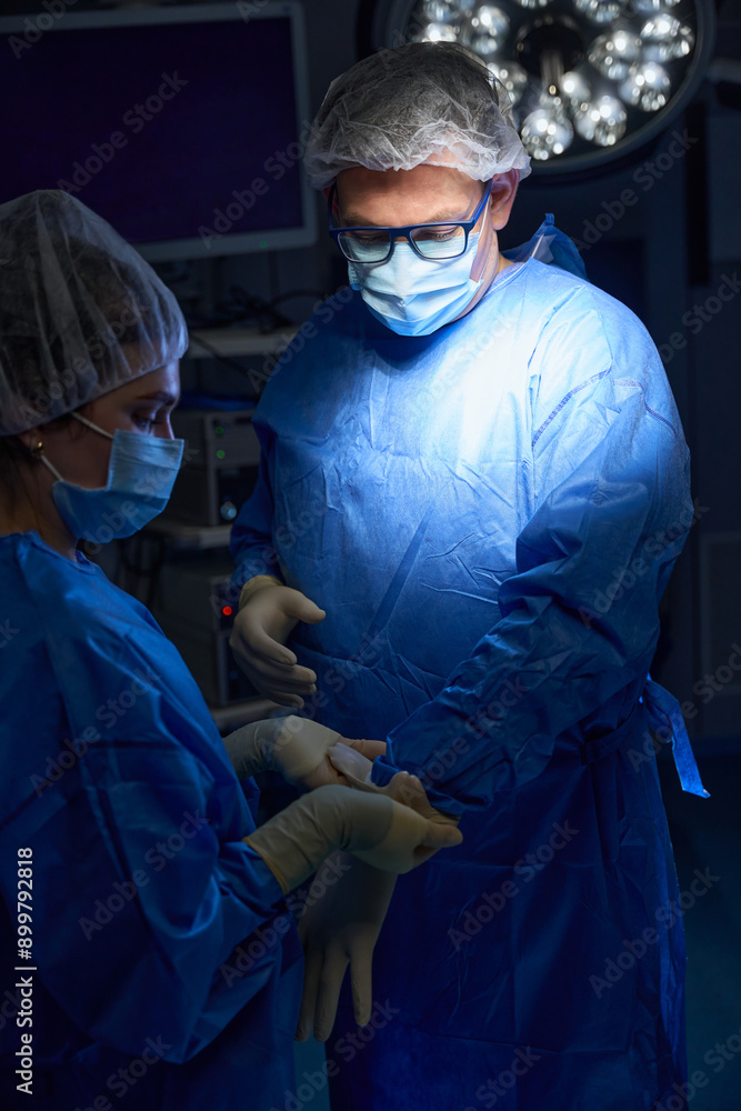 Nurse helping doctor into gloves standing in operating room Nurse helping doctor into gloves standing in operating room