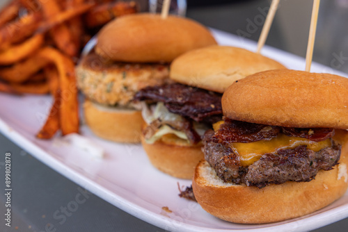 Three sliders with cheese and bacon, pulled pork and a crab cake served on buns, with a side of fries.